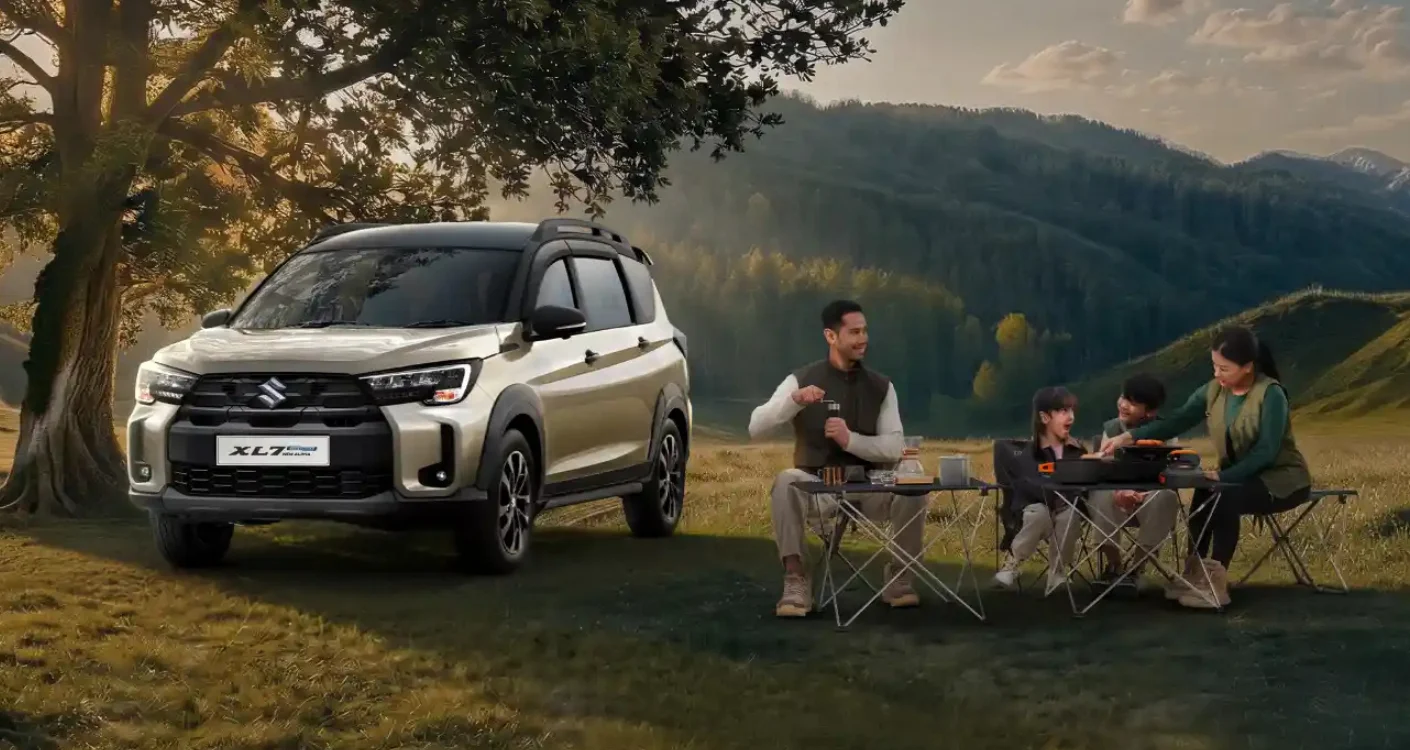 Sebuah keluarga, ayah, ibu, dan dua anak, sedang piknik di alam terbuka dengan mobil Suzuki XL7 berwarna krem yang terparkir di samping. Pemandangan perbukitan hijau di latar belakang menyiratkan keindahan alam di sekitar Kota Batam.